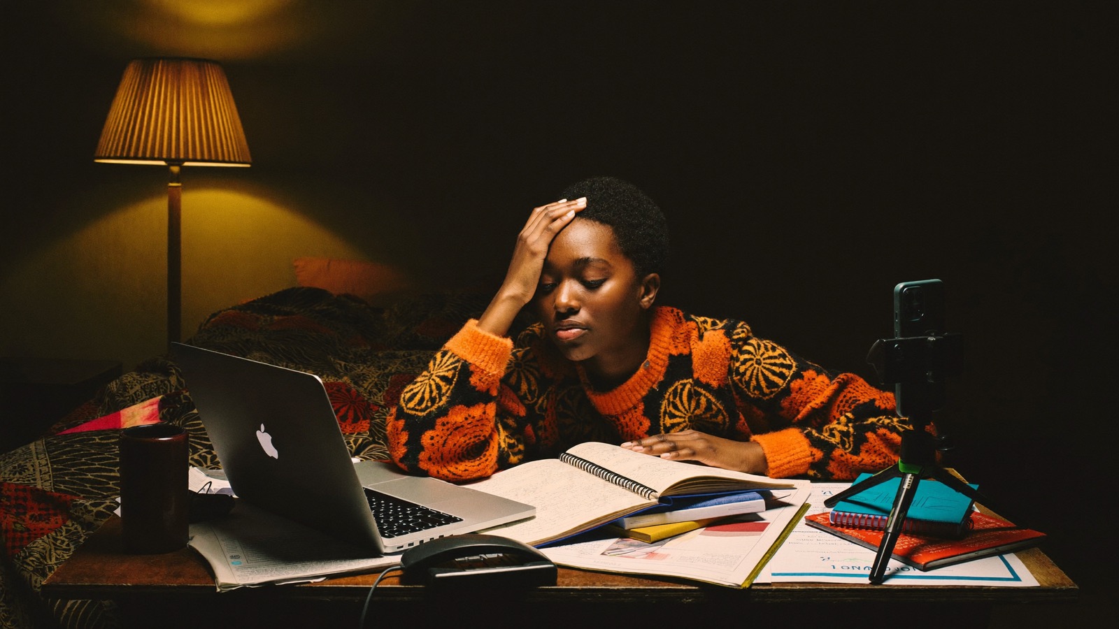 Exhausted creator working alone late at night surrounded by her laptop, phone and papers