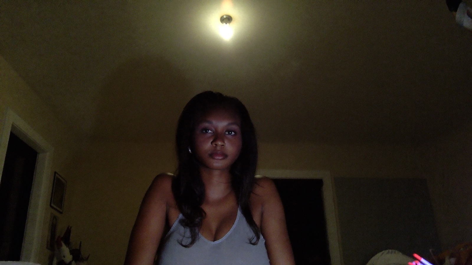 A model lit only by a single ceiling bulb above her, her face dim with dark shadows under her eyes