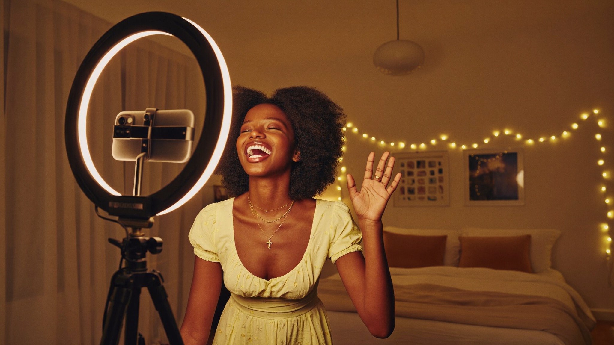 African creator laughing and waving hello at her phone on a tripod, greeting a viewer by name